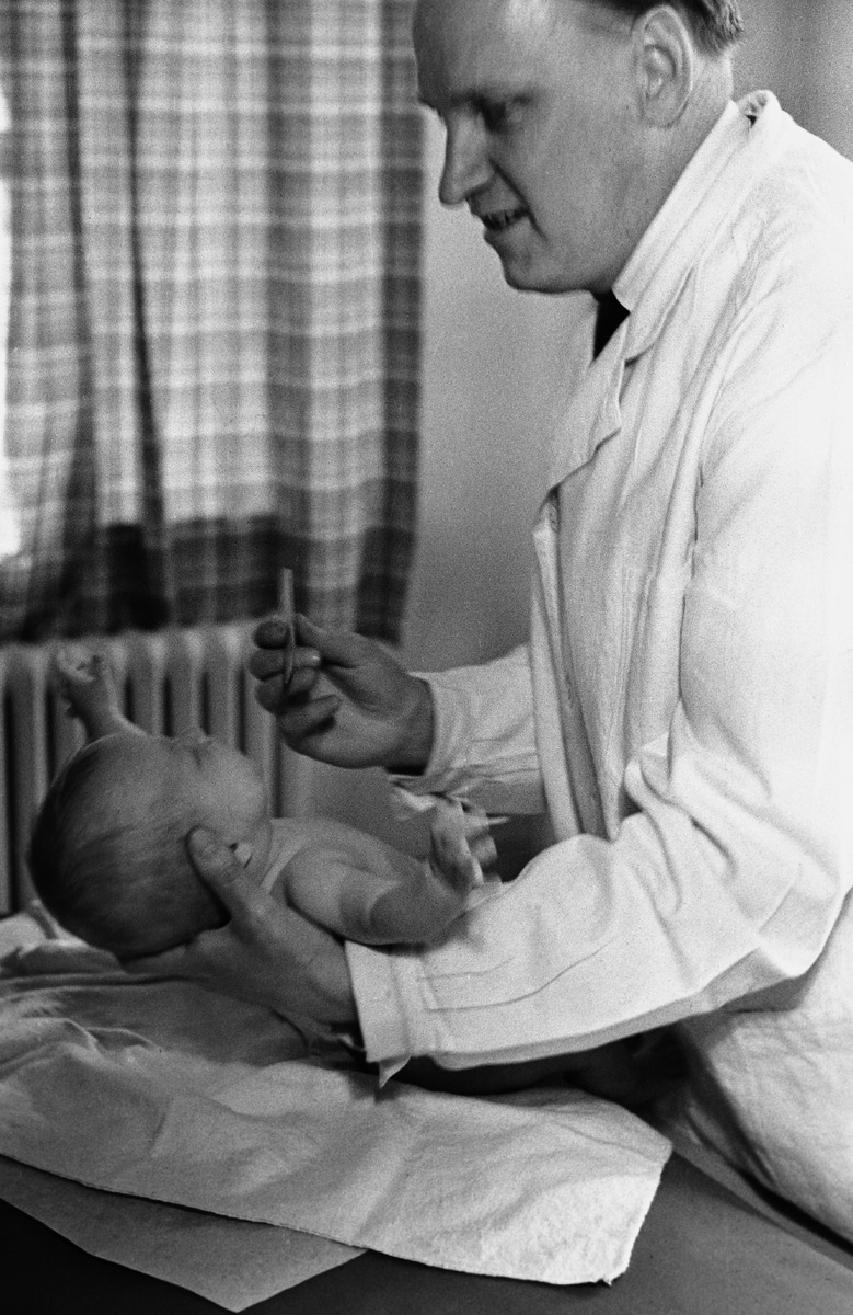 Lääkäri tutkii pehmustetulla pöydällä makaavaa vauvaa. Mustavalkoinen valokuva neuvolasta vuonna 1951.